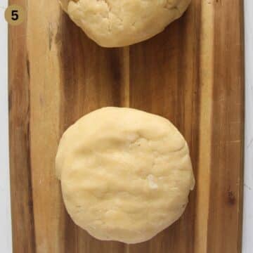 two balls of pie dough on a wooden cutting board.