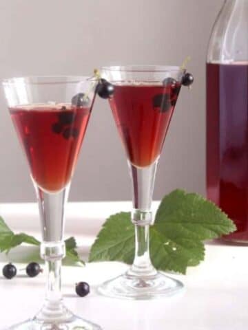 two small glasses and a large bottle with homemade creme de cassis.