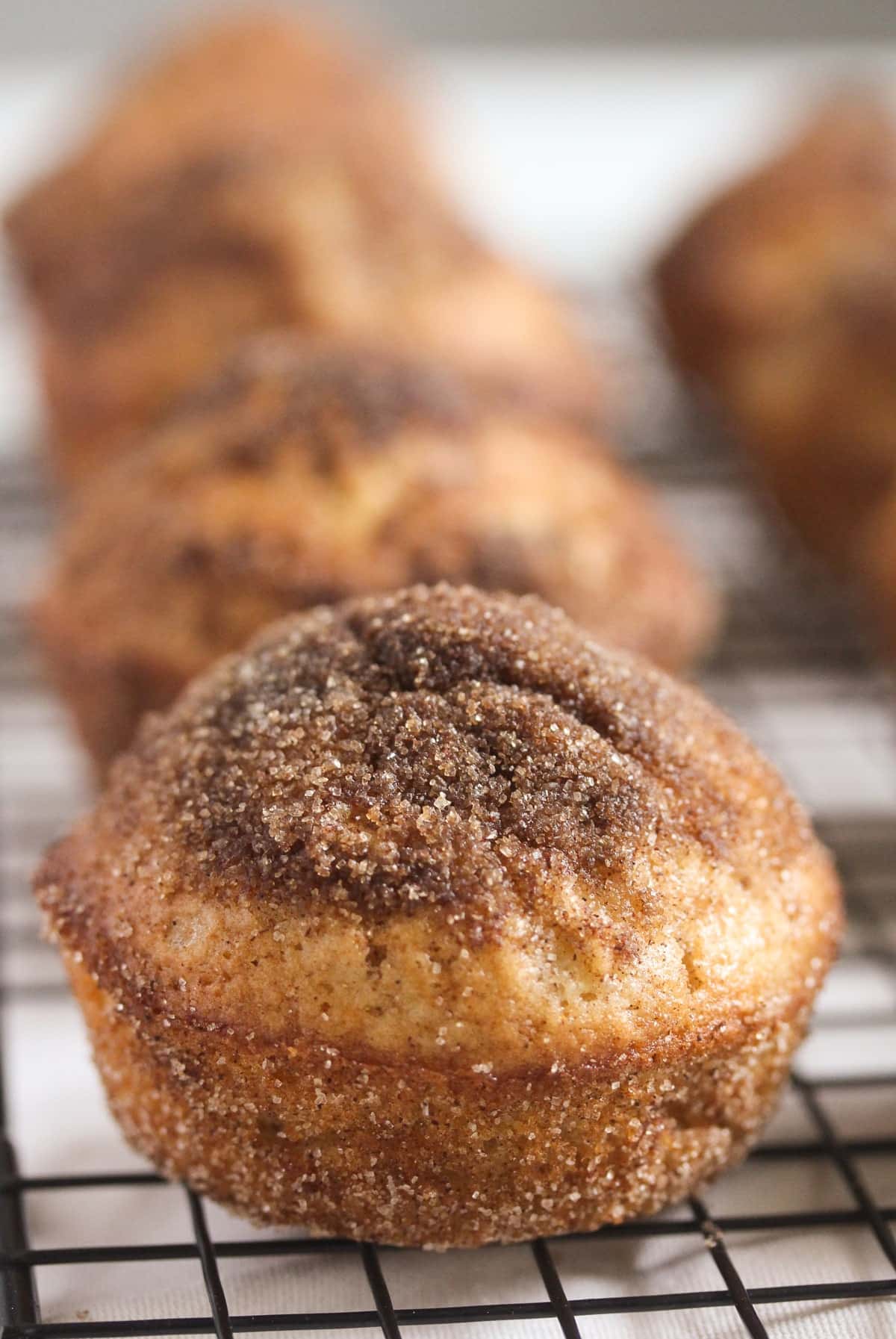 cinnamon apple donut muffin on a wire rack, a few more behind it.