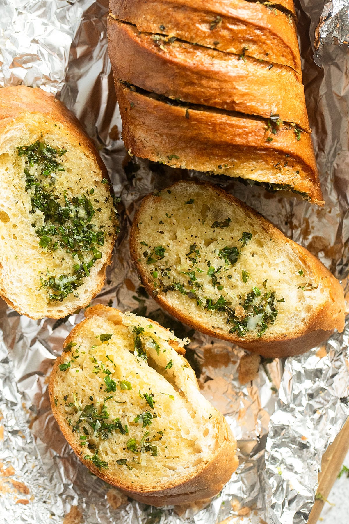 sliced baguette stuffed with garlic butter and fresh herbs on aluminum foil.