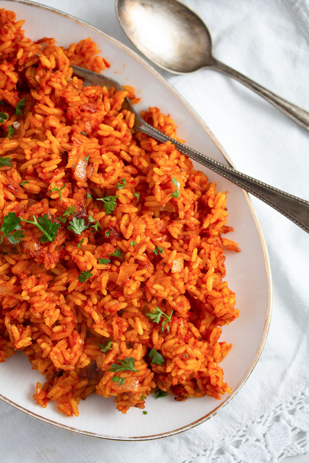 bright orange jollof rice nigerian style on a platter with fork and spoon.