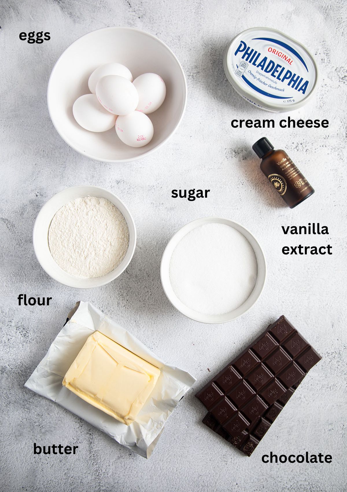 labeled ingredients for making brownies with cream cheese, chocolate, sugar, flour, eggs, butter and vanilla.