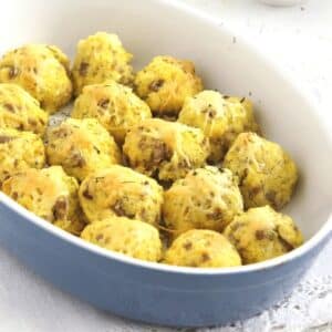 many polenta cheese balls with sausage in a small baking dish sprinkled with cheese.
