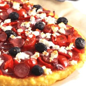 polenta pizza topped with pepperoni, olives, tomatoes, and feta.