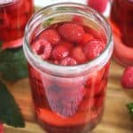 preserved raspberries in sugar syrup in a tall jar, some other jars behind it.