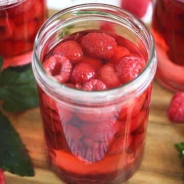 preserved raspberries in sugar syrup in a tall jar, some other jars behind it.