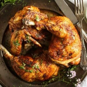 golden brown and crispy roasted half chicken pieces on a vintage platter with fork and knife.