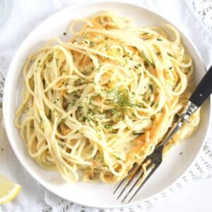 creamy veggie pasta on a white plate with a spoon.