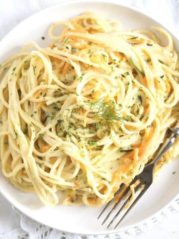 creamy veggie pasta on a white plate with a spoon.