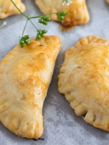 two spicy beef empanadas and a cilantro sprig with seeds.