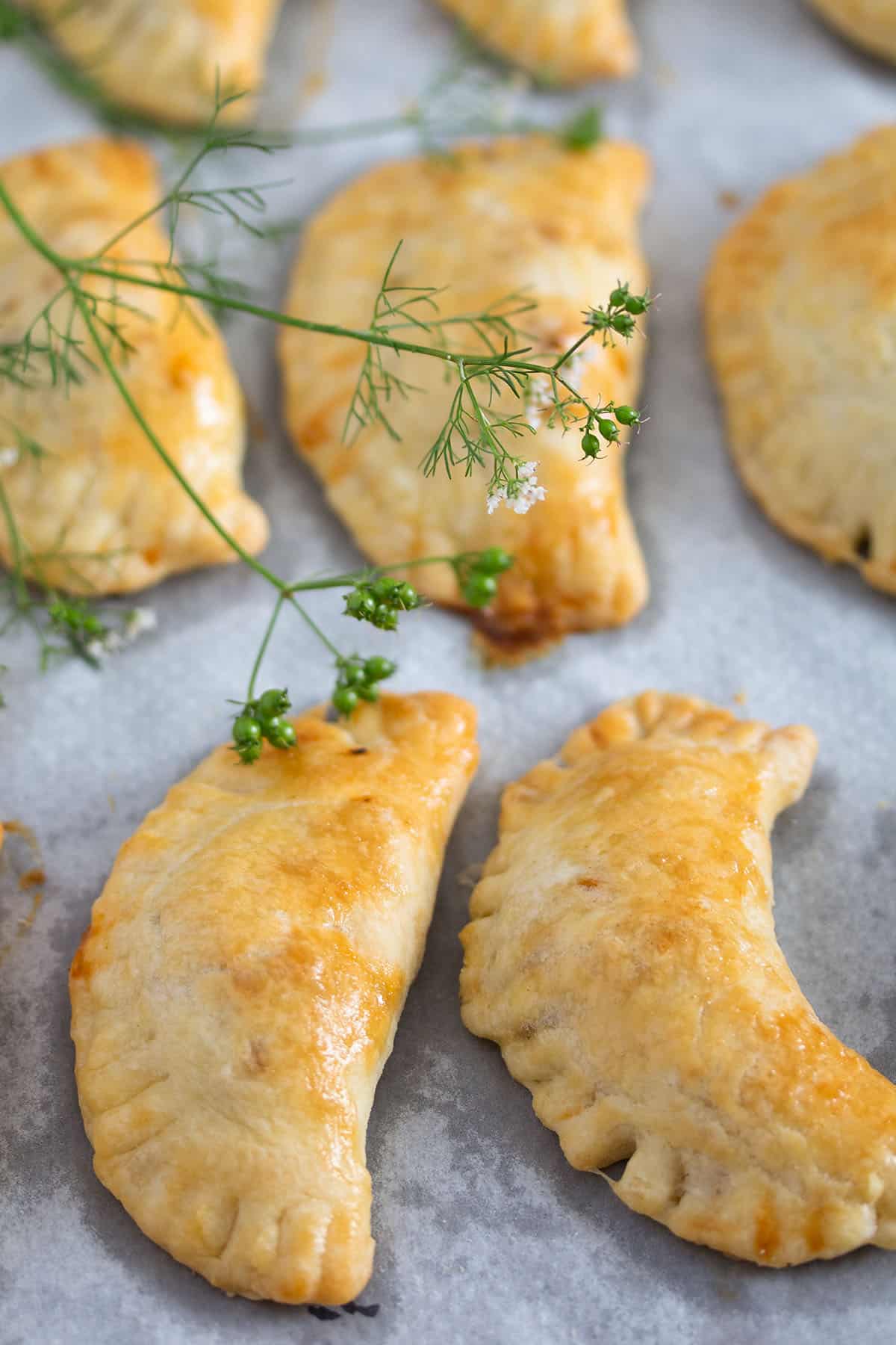 many spicy beef empanadas on a baking sheet lined with parchment paper.