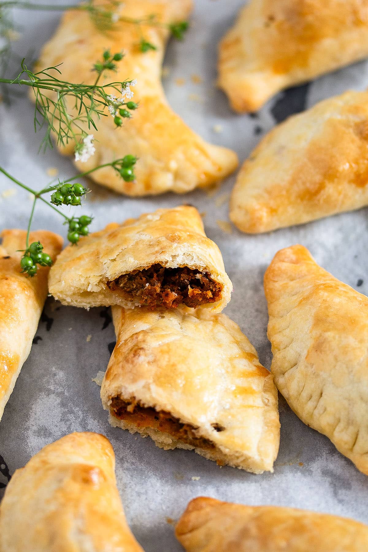 many empanadas with spicy beef, one cut in half to show the filling.