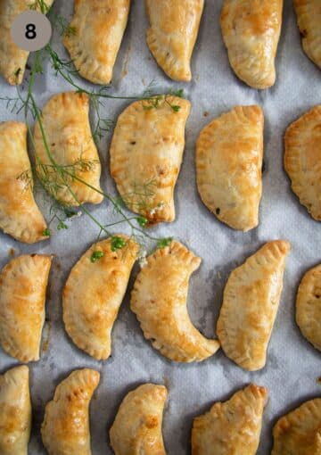 many golden baked empanadas with beef on a baking sheet.