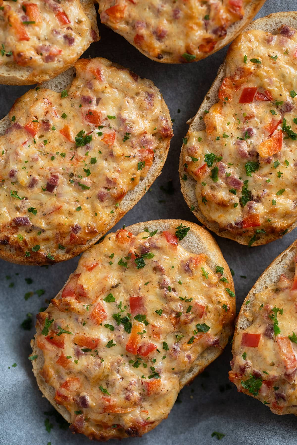 many bread rolls topped with ham and cheese and baked in the oven.