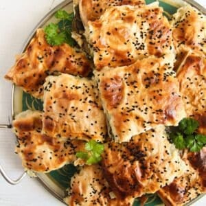 pieces of turkish spinach pie stapled on a round platter and sprinkled with parsley.