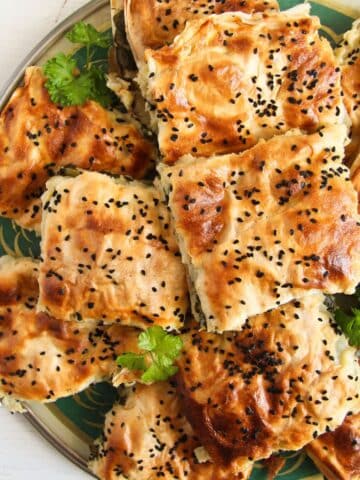 pieces of turkish spinach pie stapled on a round platter and sprinkled with parsley.