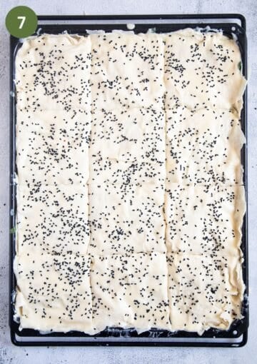 unbaked spinach pie sprinkled with nigella seeds in a baking tray.