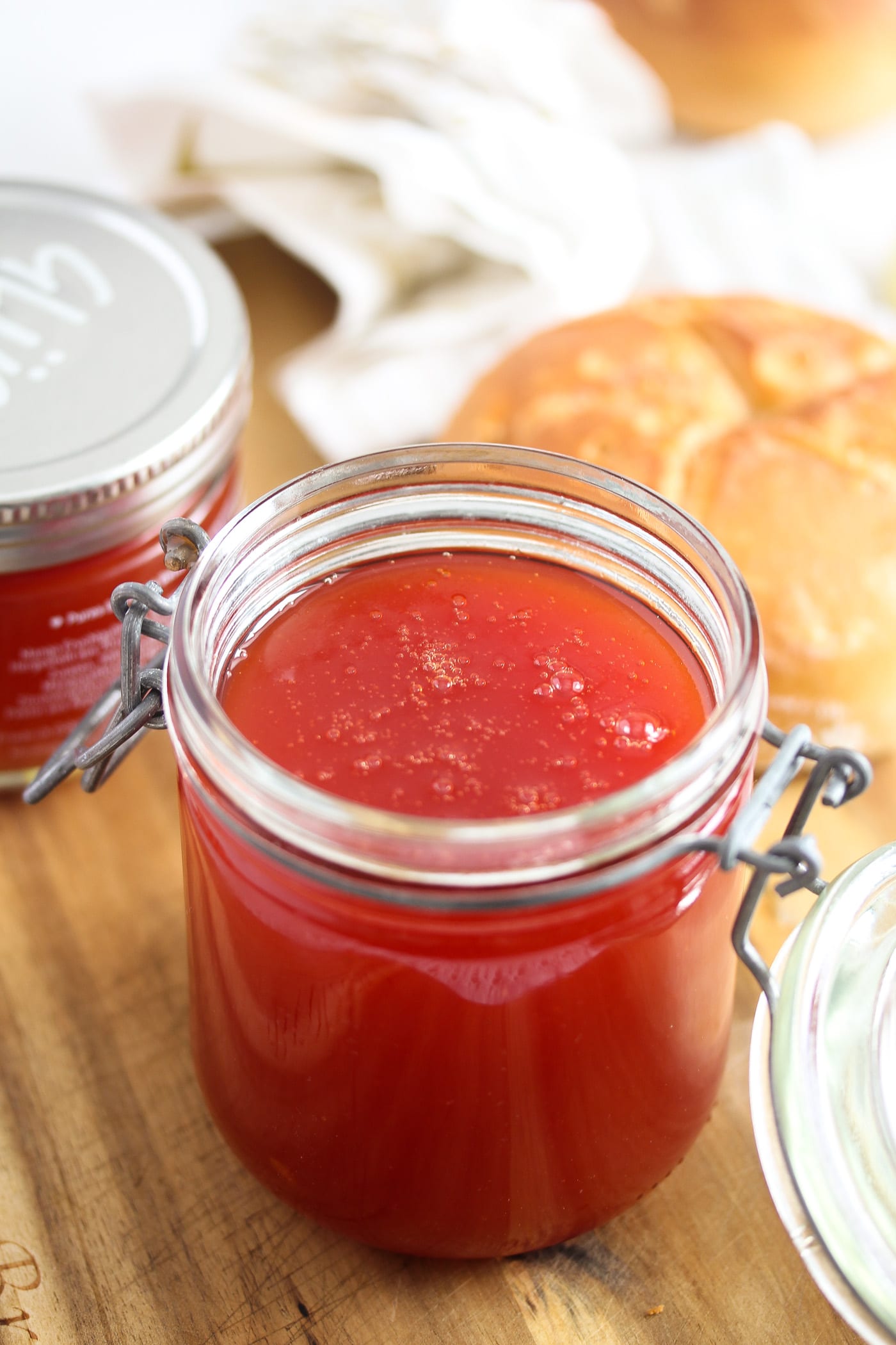red jelly in a jar with bread rolls behind