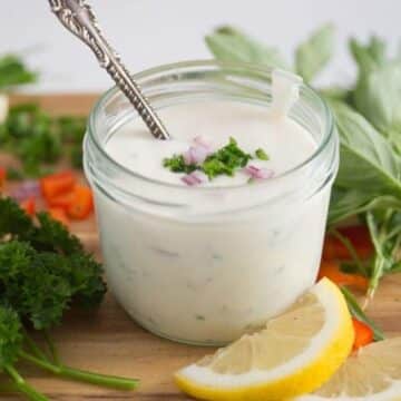 jar with greek yogurt dressing, lemon slices and herbs around it.