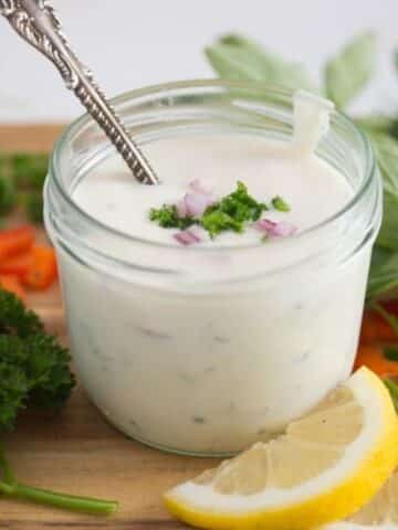 jar with greek yogurt dressing, lemon slices and herbs around it.