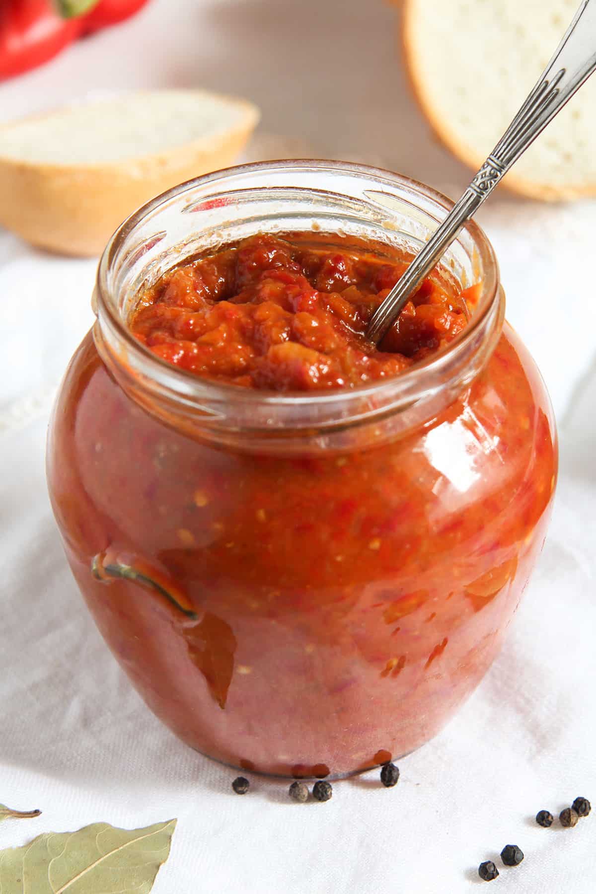 jar of romanian zacusca with a spoon in it, white bread behind it.