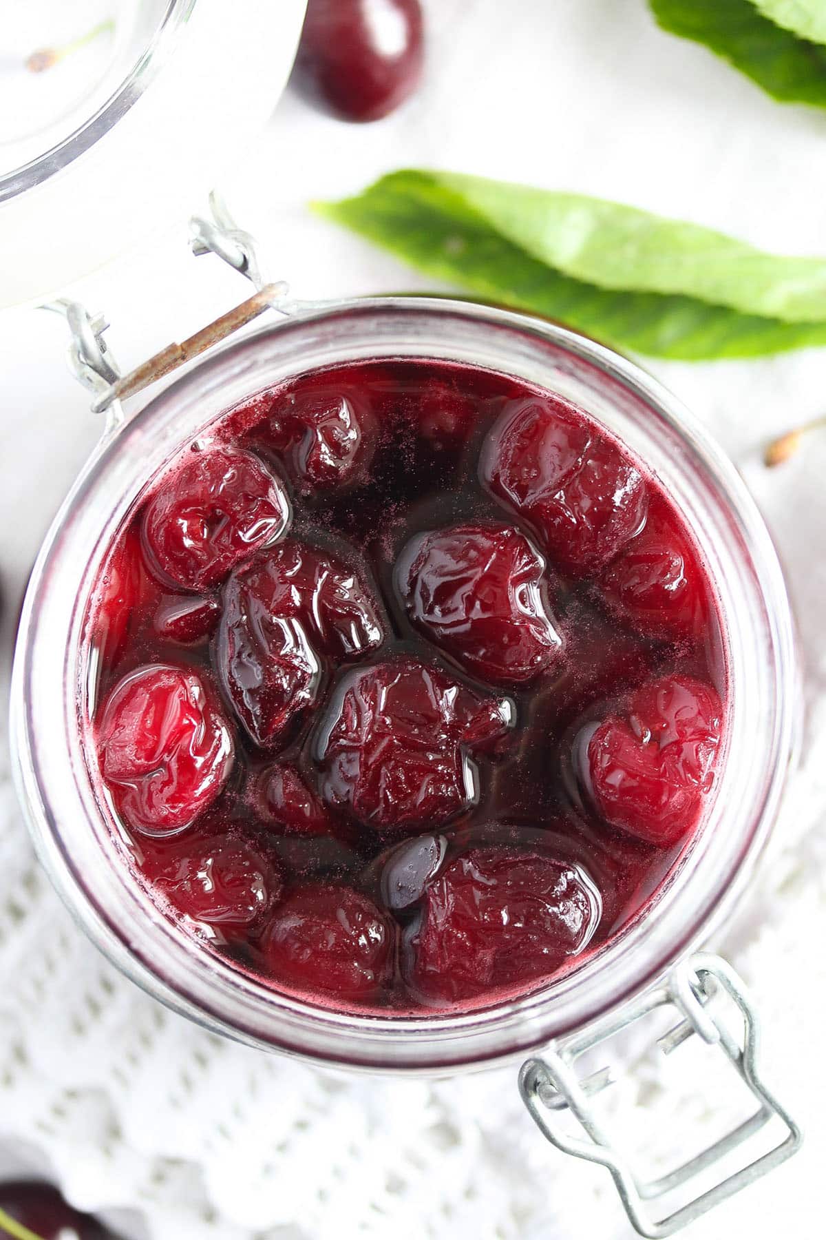 canned amaretto cherries in a jar with cherry and leaves around the jar.