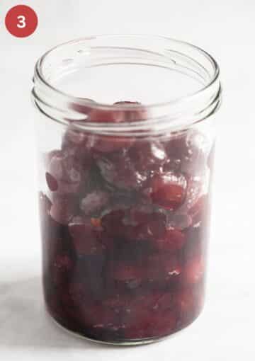 filling amaretto cherries in a tall jar.