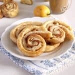 three apple puff pastry rolls on a plate and an apple behind it.