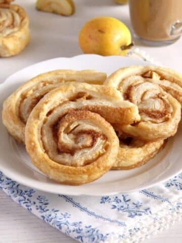 three apple puff pastry rolls on a plate and an apple behind it.