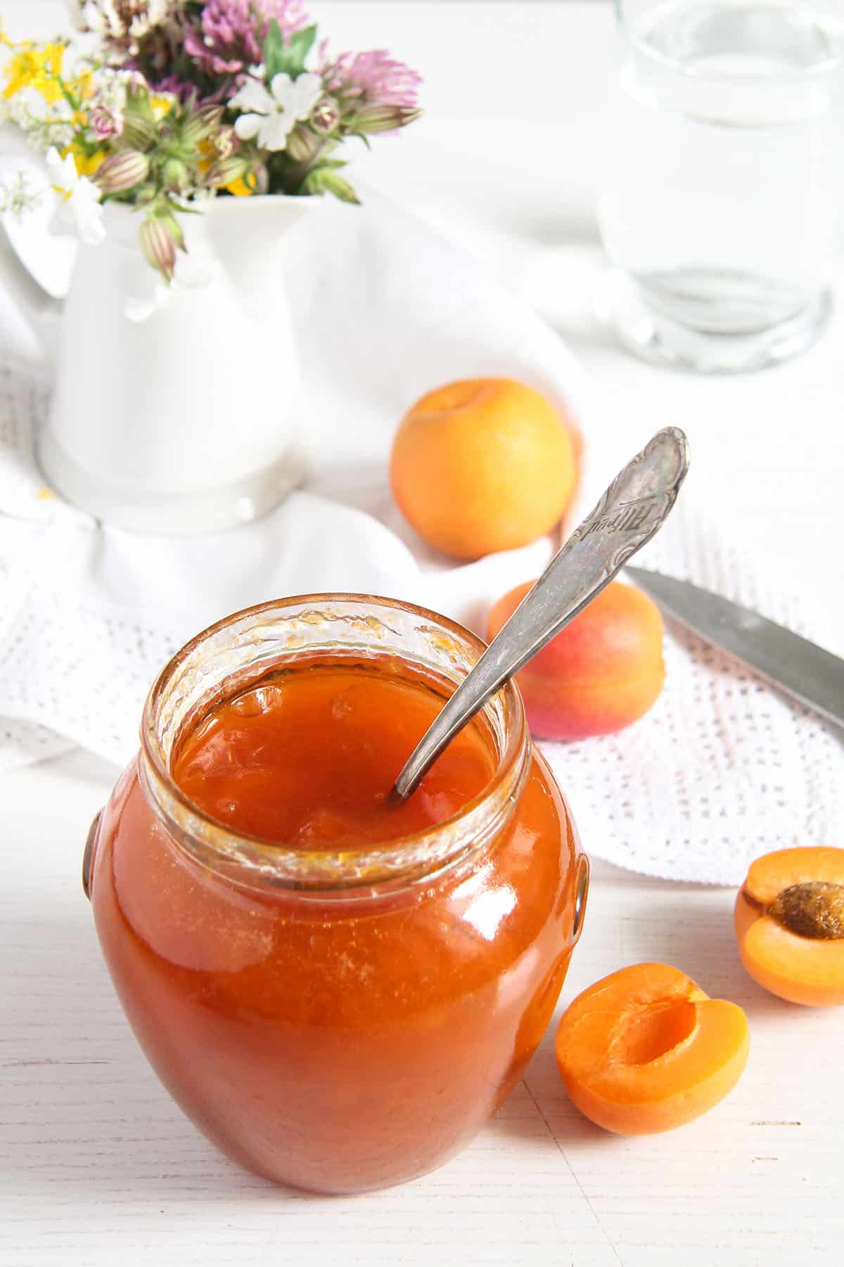 small jar of jam with a spoon in it and a few small apricots around it.