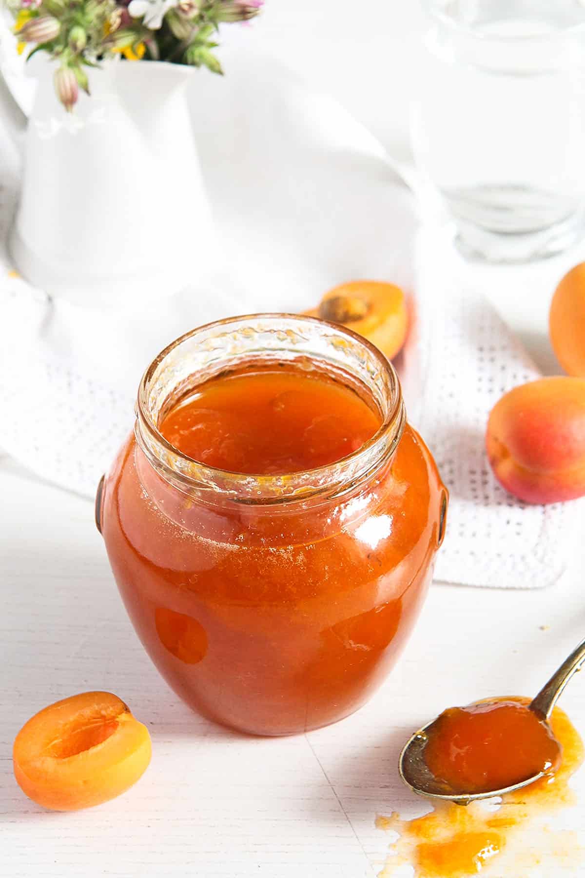 apricot jam in a small jar and on a spoon spilling on the table.