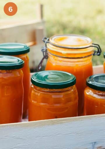 different-sized apricot jam jars cooling in a wooden box.