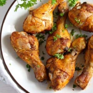 many baked chicken drumsticks sprinkled with parsley on a plate.