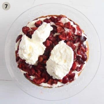 adding dollops of whipped cream to bakewell cake with cherries.