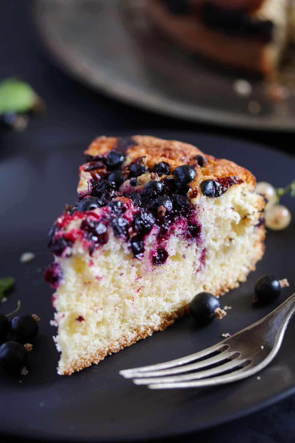 one slice of moist and fluffy blackcurrant cake on a black plate with a fork.