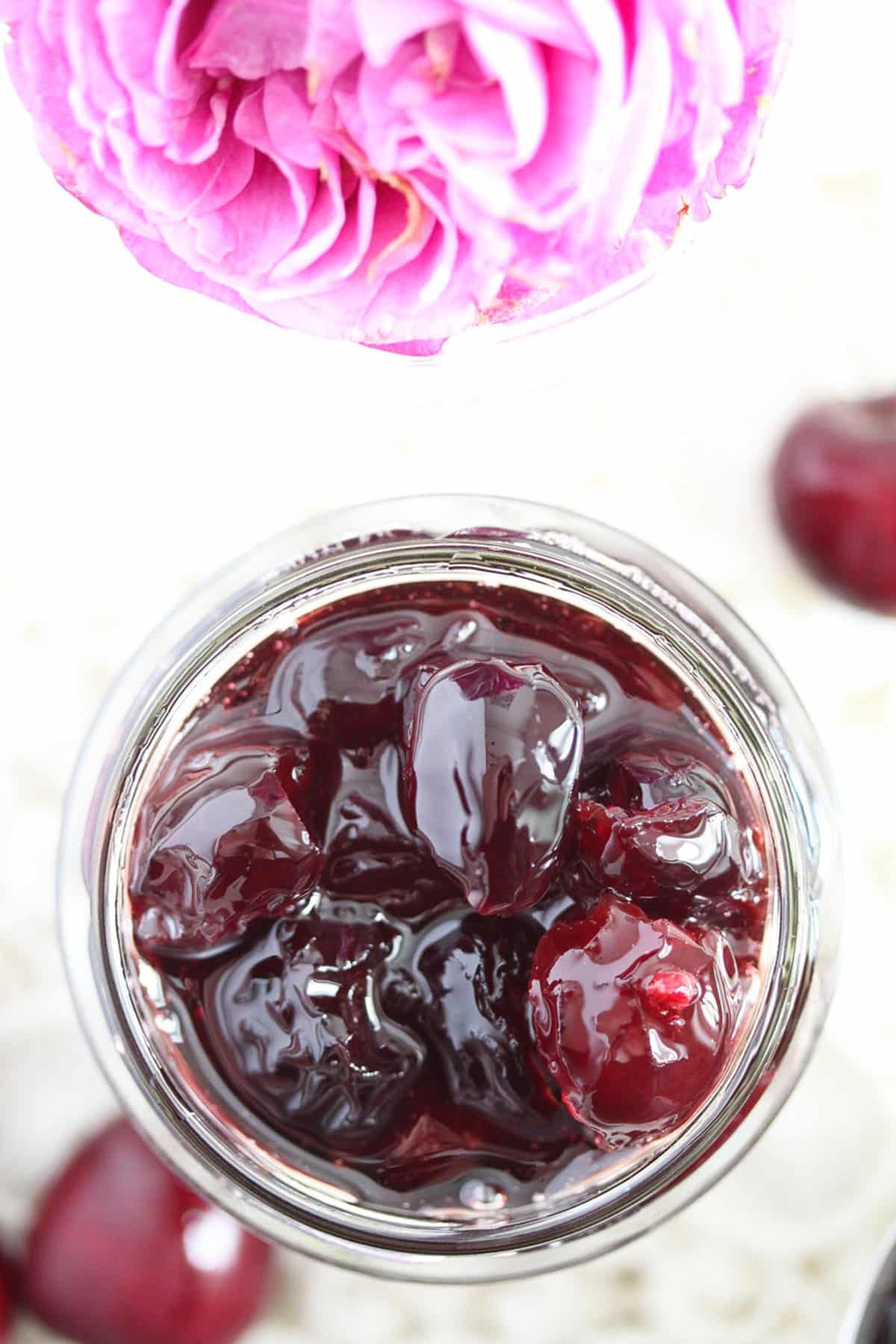a jar of glossy candied cherries and pink wild rose beside it.