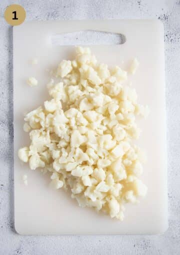 chopped cooked cauliflower on a cutting board.