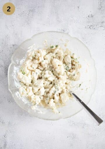 mixing cauliflower florets with mayonnaise with a spoon in a bow.