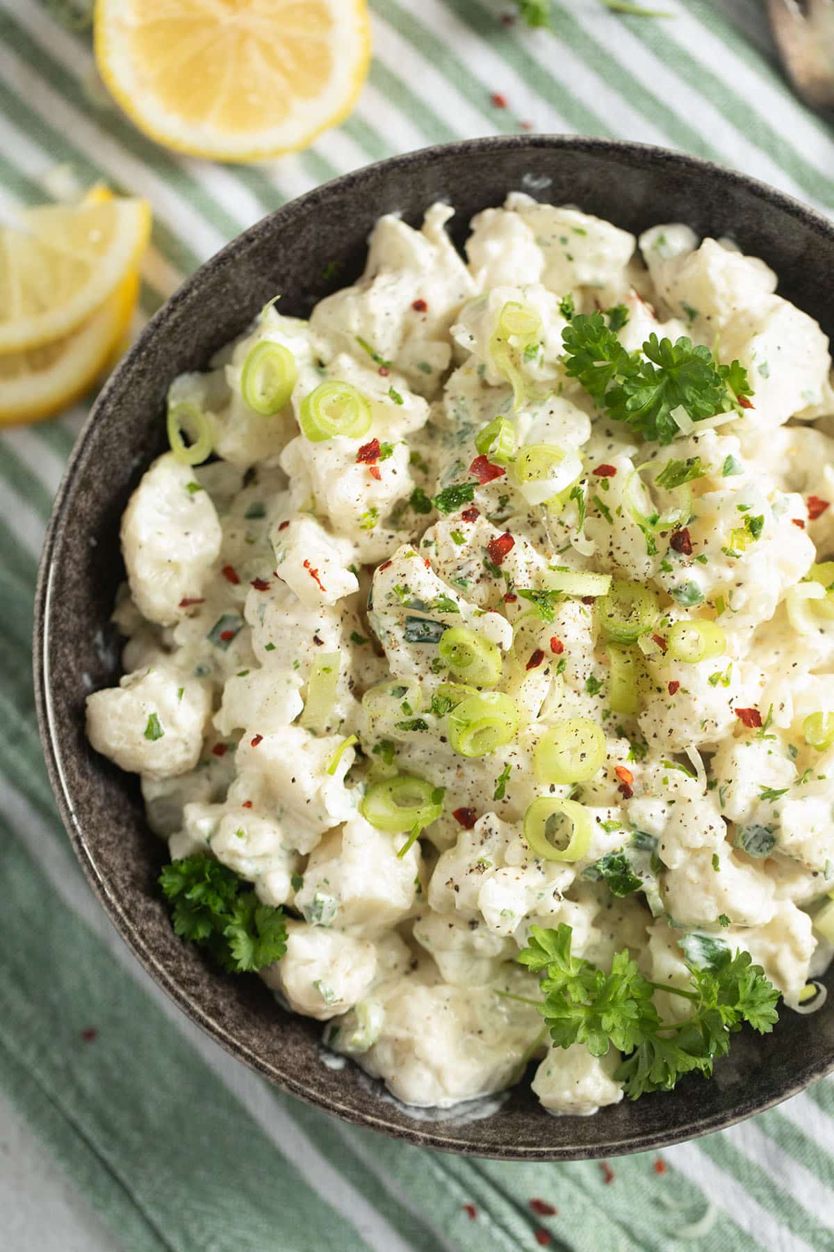 cauliflower salad with mayonnaise, topped with green onions in a bowl. 