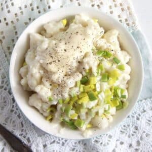 bowl of cauliflower salad with mayonnaise, topped with finely chopped leeks.