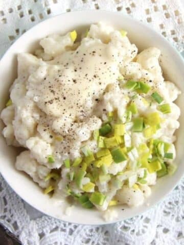bowl of cauliflower salad with mayonnaise, topped with finely chopped leeks.