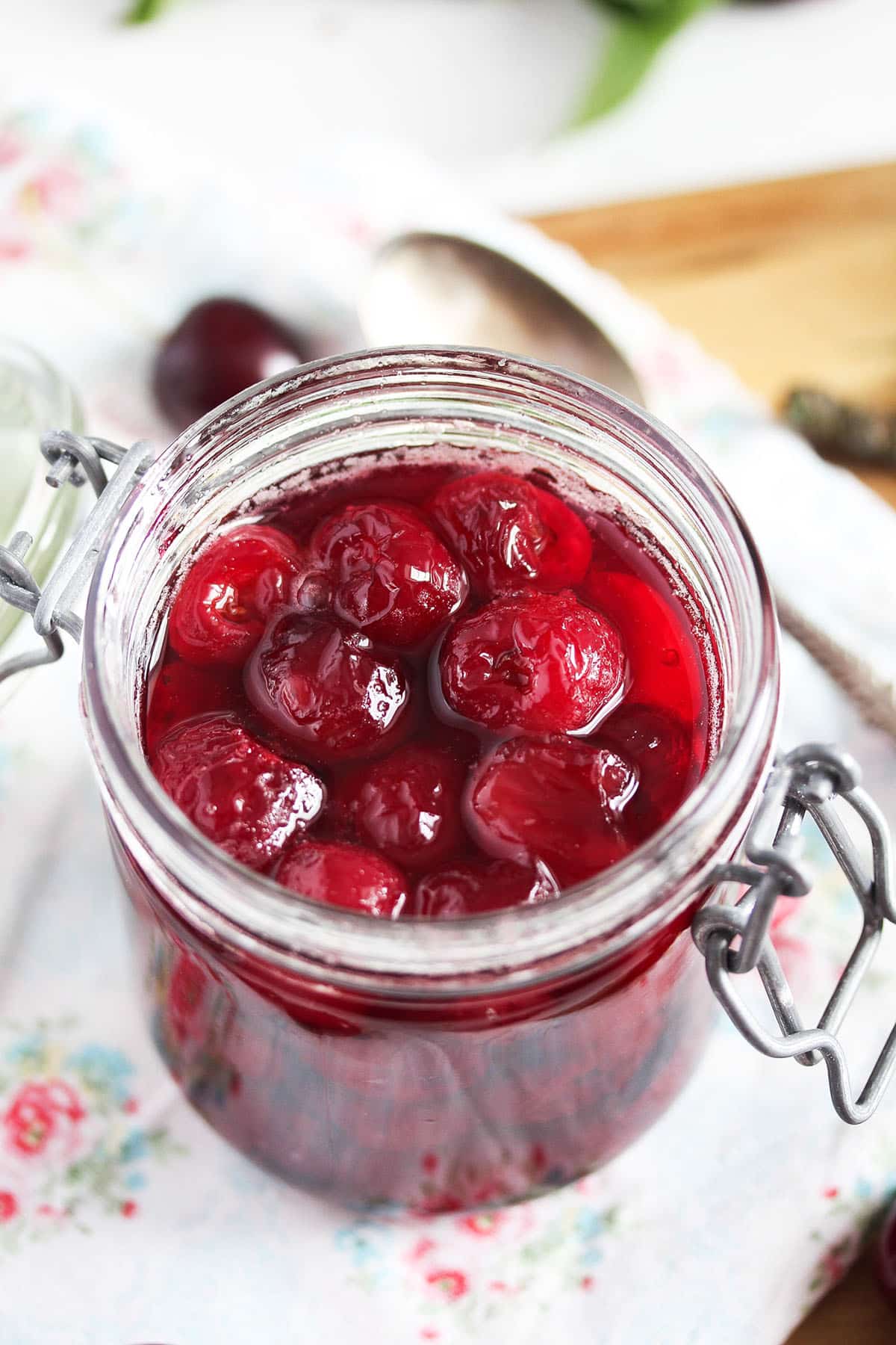 a small jar with kirsch cherries on a kitchen cloth with flowers on it.