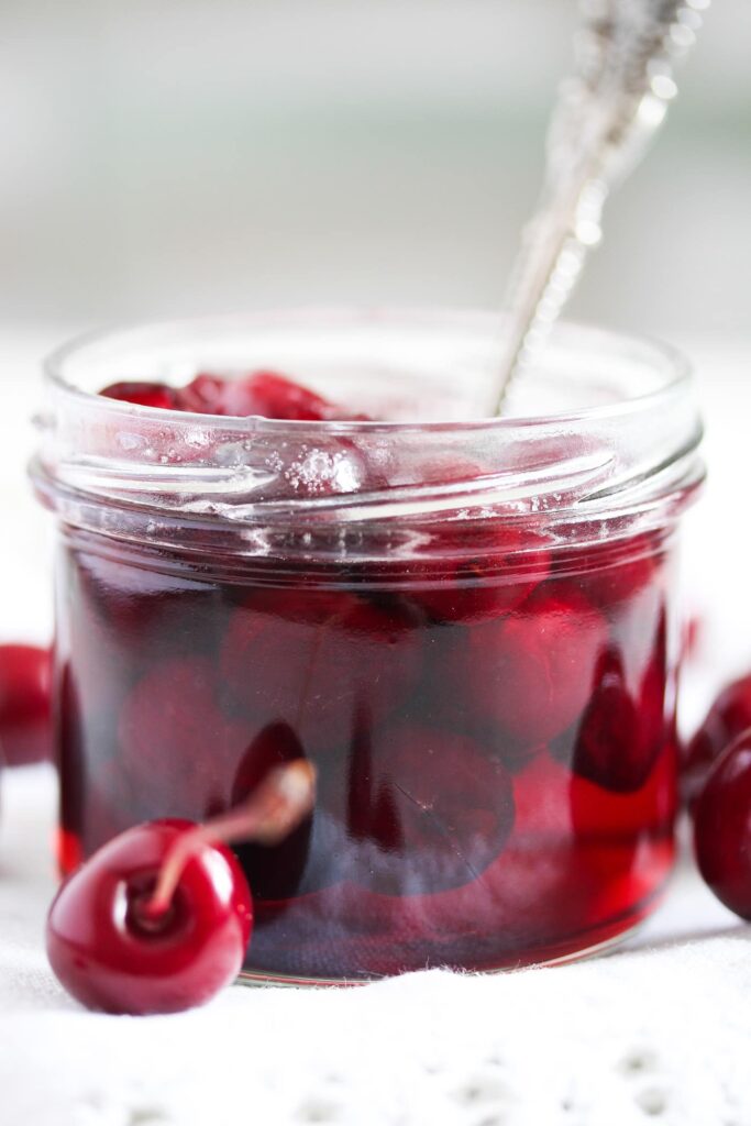 small jar with floating cherries and a spoon