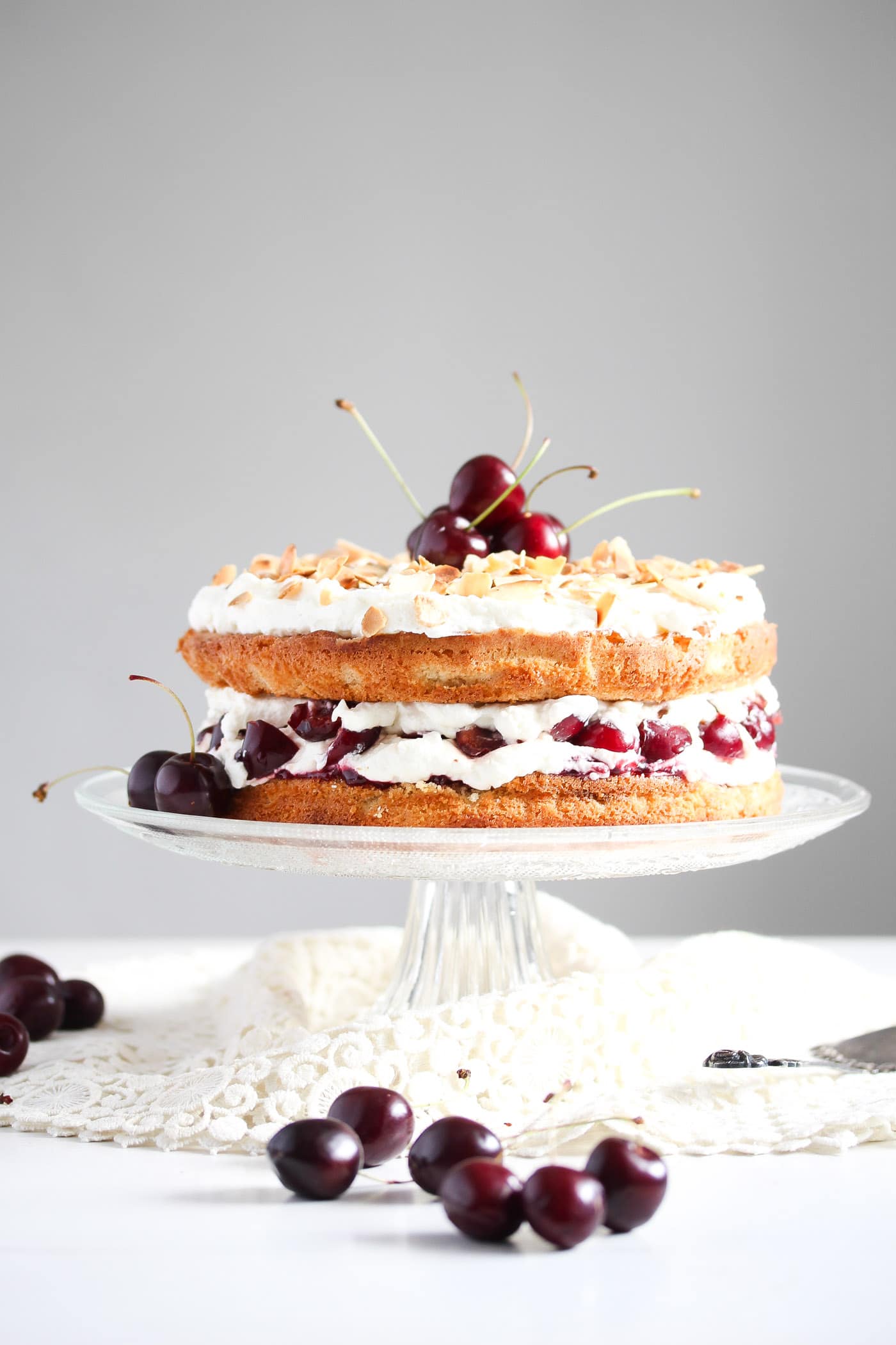 cherry bakewell cake on a tall cake platter with fresh cherries