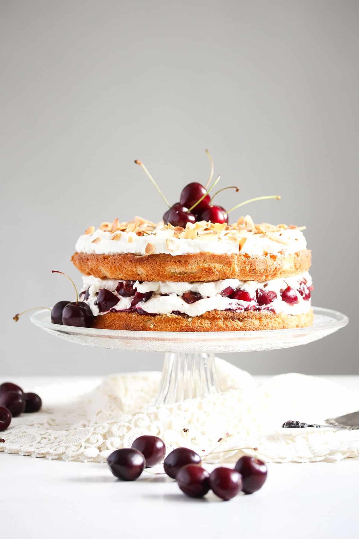 cherry bakewell cake on a high cake platter and some cherries around it.