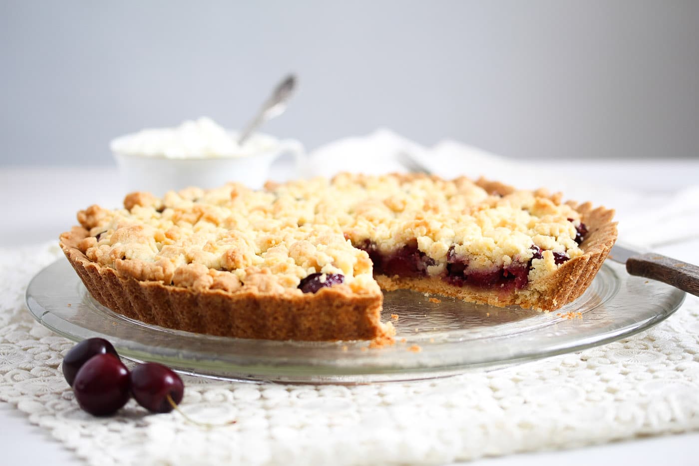 cherry crumble pie on a platter served with cream
