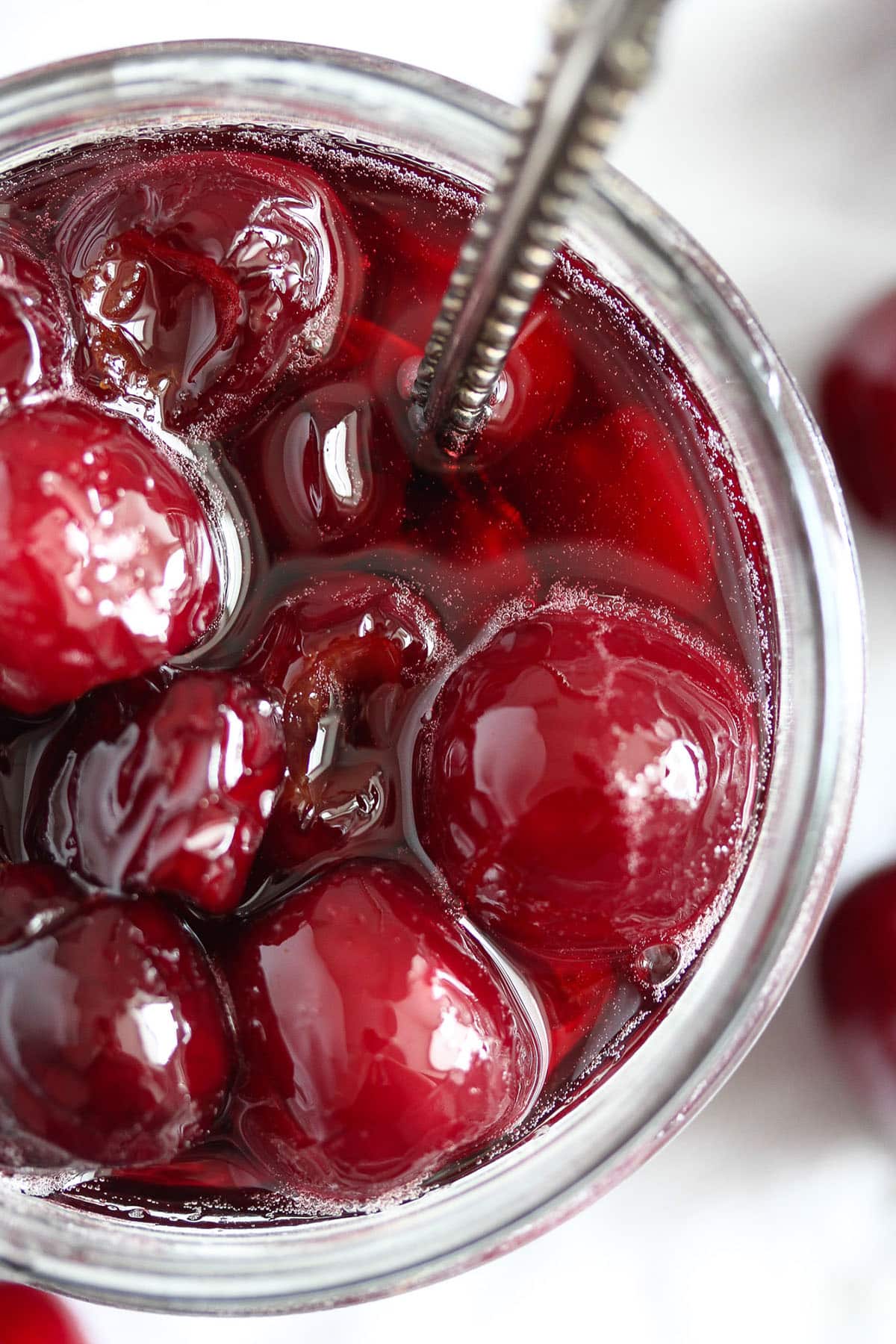 glossy cherries in syrup in a jar with a spoon in it.