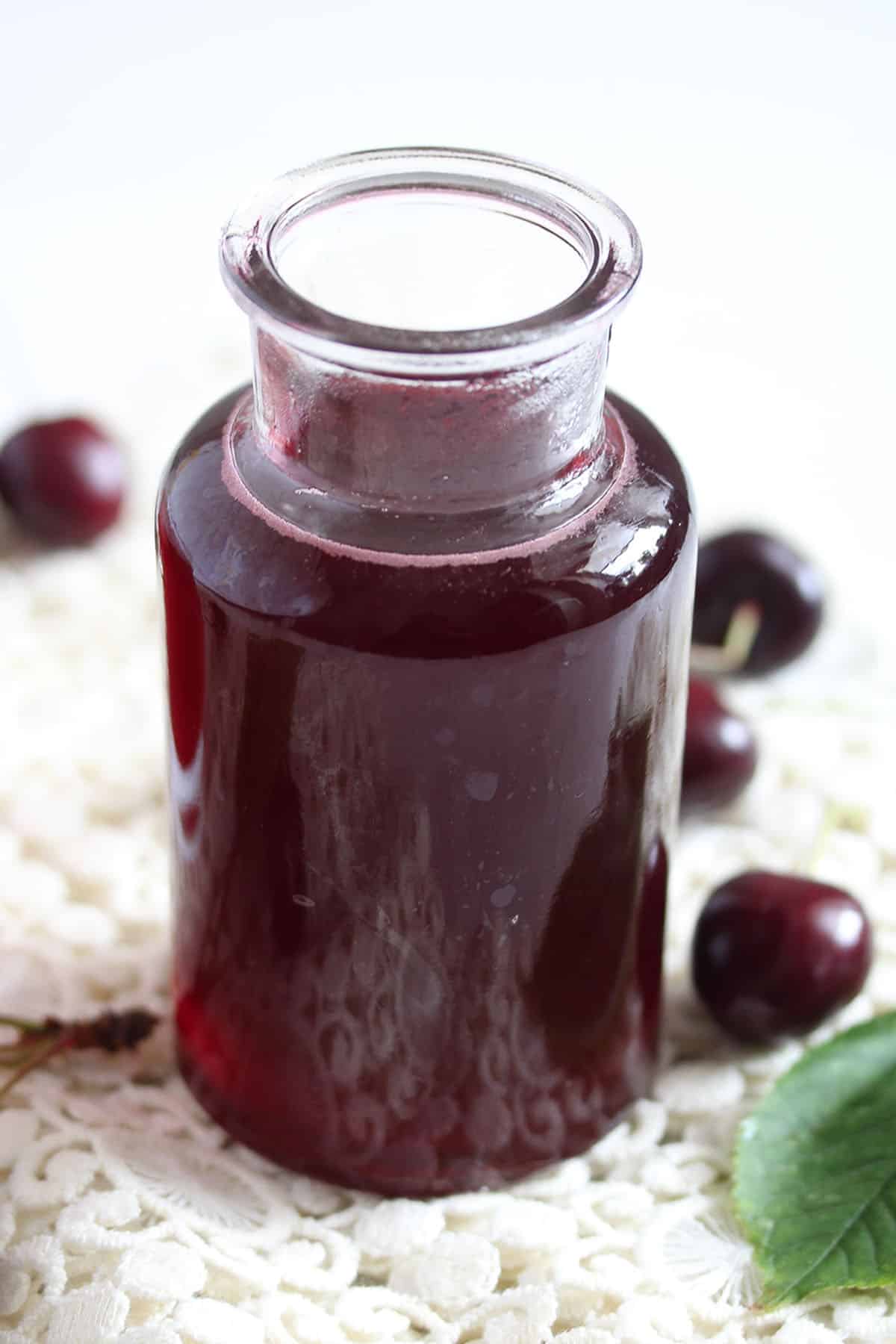 a small bottle with cherry syrup and a few cherries around it.