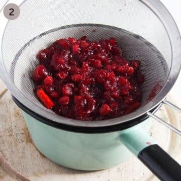 straining cooked cherries through a sieve into a small green pot.