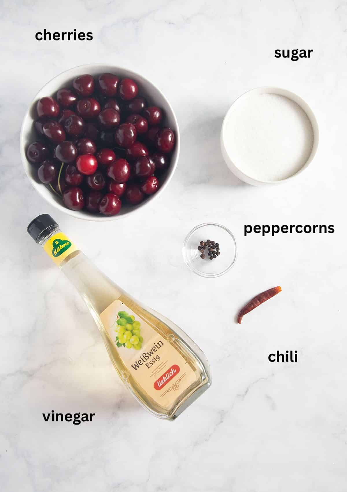 Flat lay of amaretto cherry ingredients with labels, including fresh cherries, sugar, lemon, amaretto, and flavorings.
